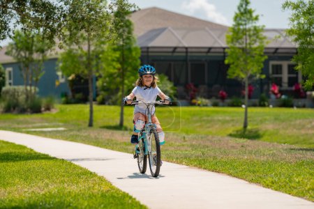 Petit garçon en vélo dans un parc d'été. Les enfants apprennent à conduire un vélo sur une allée à l'extérieur. Enfant à vélo dans la ville portant des casques comme équipement de protection. Enfant à vélo extérieur