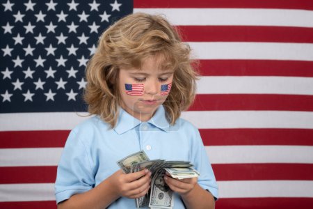 Téléchargez les photos : Concept de billets en dollars américains. Portrait d'un enfant avec billets en dollars isolés sur fond de drapeau américain - en image libre de droit