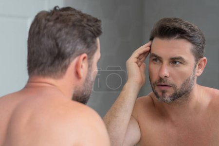 Photo for Sexy sensual man with perfect skin touch face after shaving. Skin care healthcare cosmetic procedures concept. Close up man looking in mirror, sensitive skin, cosmetology treatment. Skin care - Royalty Free Image