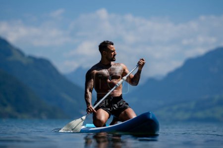 Foto de Hombre sexy con tabla de paddle. Hombre remando en el paddleboard. Musculoso hombre hispano fuerte en tabla de sup paddle surf. SUP surf en vacaciones de verano en el lago. Cuerpo húmedo muscular fuerte. Torso desnudo desnudo - Imagen libre de derechos