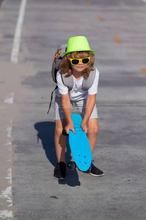 Téléchargez les photos : Un gamin qui joue au skateboard. Petit garçon à skateboard sur la route. Un gamin qui pratique le skateboard. Les enfants apprennent à faire du skateboard dans un parc lors d'une journée ensoleillée d'été. Sports d'été en plein air et mode de vie - en image libre de droit