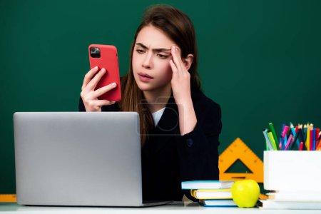 Photo for Female student using phone in classroom. School girl chatting on mobile phone near blackboard. College student learning in college classroom. Education concept. Lesson and homework in university - Royalty Free Image