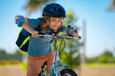 Foto de Niño pequeño montando en bicicleta en el parque de verano. Un niño conduce una bicicleta en un camino de entrada afuera. Un chico montando bicicletas en la ciudad usando cascos. Niño en bicicleta al aire libre. Bicicleta para niños en el vecindario americano - Imagen libre de derechos