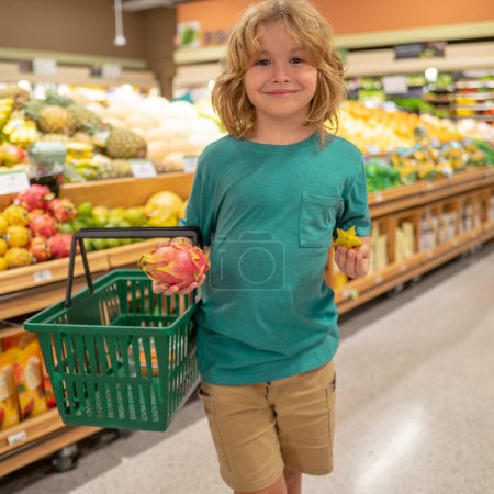 Foto de Niño con frutas. El niño está eligiendo verduras y frutas frescas en la tienda. Niño comprando comida en supermercado de comestibles - Imagen libre de derechos