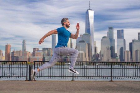 Foto de Corre. Un hombre sano corriendo en la ciudad de Nueva York. Deporte de fitness, corredor de hombres está corriendo cerca de Manhattan. Un hombre corriendo por la calle americana. Un hombre corriendo en Nueva York con ropa deportiva. Ropa deportiva para corredores maduros - Imagen libre de derechos