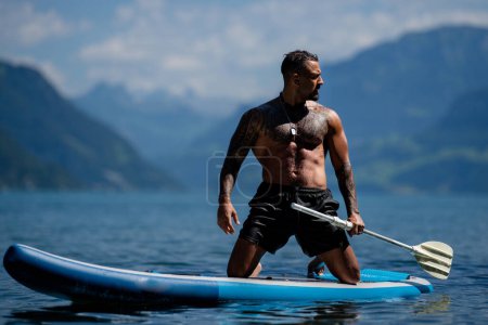 Foto de Un hombre relajado en el lago. Hombre guapo con torso desnudo en la playa de verano. Retrato de un hombre sexy en un lago de los Alpes. Libertad y aventura de viaje. Viajero sexy está disfrutando del paisaje en Suiza - Imagen libre de derechos