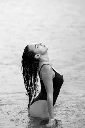 Foto de Lluvia de verano. Mujer en bikini Disfrutando del clima lluvioso. Modelo de bikini de verano. Chica sexy en la playa del mar. Concepto de libertad y despreocupación. Fit sexy mujer descanso en verano agua en la lluvia - Imagen libre de derechos