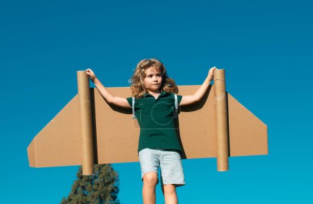 Photo for Boy child with wings at sky imagines a aviator pilot and dreams of flying. Kid boy plays pilot with cardboard toy airplane in the park - Royalty Free Image