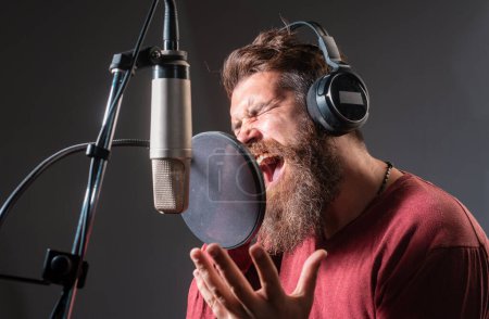Cantante en un estudio de grabación. Expresivo hombre barbudo con micrófono. Productor de sonido. Karaoke signer, vocalista musical