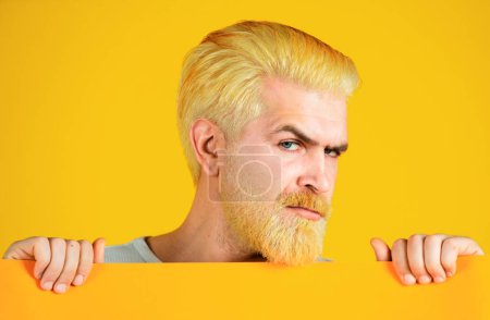 Kaukasische blonde männliche Modell posiert in Mode-Konzept-Studio-Shooting. Glücklicher Mann mittleren Alters, der leeres Papier präsentiert. Mann zeigt gelbes Blanko-Papier