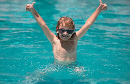 Téléchargez les photos : Mignon enfant garçon mains levées nager dans la piscine, fond d'eau d'été avec espace de copie. Visage drôle d'enfants - en image libre de droit