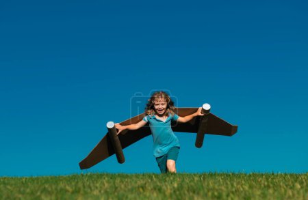 Photo for Happy child with paper wings against blue sky. Kid with toy jetpack having fun in spring green field outdoor. Freedom carefree and kids imagination dream concept - Royalty Free Image