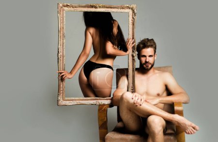 Photo for Portrait of a young woman holding a frame. Couple. Sensual woman with perfect body in black lingerie standing near muscular man. Pose for family portrait. Valentines day. Romantic and love - Royalty Free Image