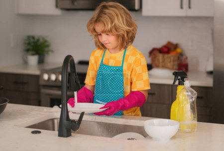 Téléchargez les photos : Nettoyage. Enfant garçon laver la vaisselle dans l'évier de la cuisine. Détergents et accessoires de nettoyage. Service de nettoyage. petit garçon ménage - en image libre de droit