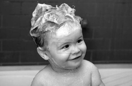 Foto de El bebé se baña en un baño con espuma y burbujas de jabón. Niños divertidos se enfrentan de cerca - Imagen libre de derechos