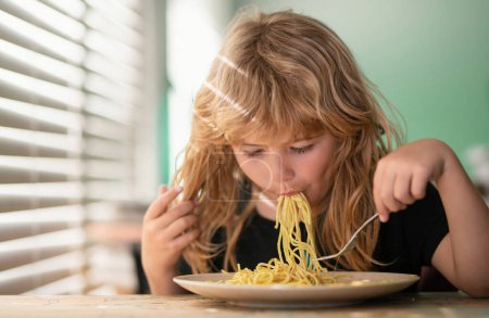 Téléchargez les photos : Tasty food, messy child eating spaghetti Close up portrait of funny kid eating. Little boy having breakfast in the kitchen - en image libre de droit