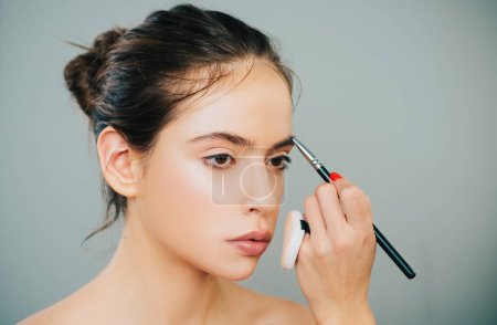 Beautiful young woman getting eyebrow make-up. The artist is applying eyeshadow on her eyebrow with brush. Young model girl getting her natural eyebrow makeup