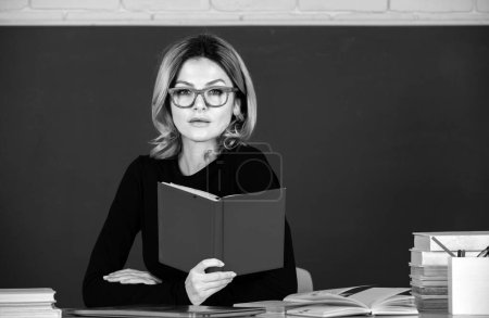 Photo for Sensual student woman in eyeglasses near blackboard. Sexy girl sit on table on chalkboard. Attractive female teacher in college. Study concept - Royalty Free Image