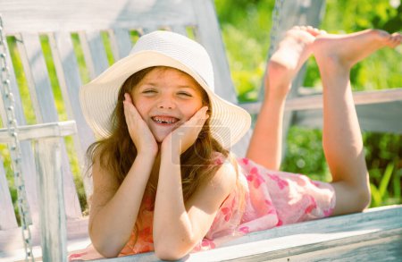 Child swing on backyard. Kid playing oudoor. Happy cute little girl swinging and having fun healthy summer vacation activity. Close up portrait of a beautiful girl in hat dreaming