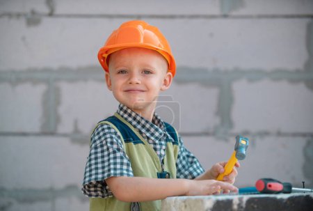 Photo for Child play with supplies, tools saw, hammer, screwdriver, helmet, builder, carpenter. Kids playing in the profession. Happy smiling little repairman. Kid boy in helmet with repair tools - Royalty Free Image