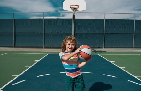 Foto de Pequeño caucásico deportes niño jugando baloncesto celebración pelota con feliz cara - Imagen libre de derechos