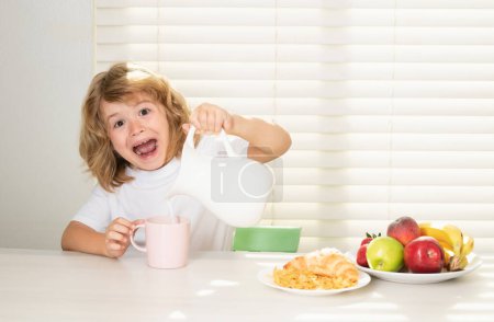 Photo for Fuuny excited little boy pouring whole cows milk for breakfast. Schoolkid eating breakfast before school. Portrait of child sit at desk at home kitchen have delicious tasty nutritious breakfast - Royalty Free Image