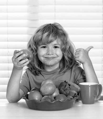 Téléchargez les photos : Un gamin qui mange des pommes. Portrait de l'enfant manger des aliments sains frais dans la cuisine à la maison. Petit garçon petit déjeuner avant l'école - en image libre de droit