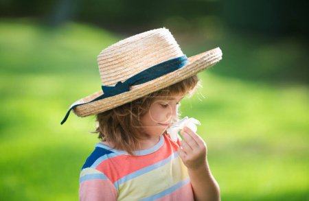 Photo for Portrait of a cute child boy in straw hat smelling plumeria flower. Close up caucasian kids face. Closeup head of funny kid - Royalty Free Image