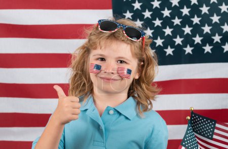 Téléchargez les photos : Kid célébration indépendance jour 4 juillet. Concept des États-Unis d'Amérique. Enfant avec drapeau américain. Jour du Souvenir. Visage drôle d'enfants avec drapeau américain sur la joue. Concept de drapeau américain - en image libre de droit