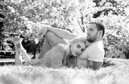 Téléchargez les photos : Couple relaxant sur l'herbe dans le parc fleuri. Concept de Saint Valentin. Couple de printemps. Portrait extérieur de jeune couple amoureux près de sakura - en image libre de droit