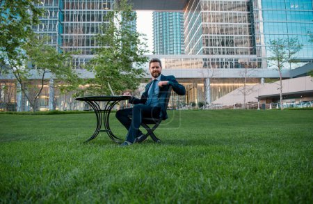 Téléchargez les photos : Homme d'affaires travaillant à distance dans un parc moderne. Portrait d'un homme d'affaires assis sur la terrasse d'un centre d'affaires moderne - en image libre de droit