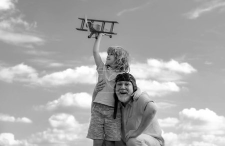 Photo for Grandson child and grandfather with toy jetpack plane against sky. Child pilot aviator with plane dreams of traveling - Royalty Free Image