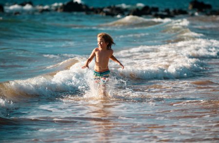 Foto de Niño corriendo a través del agua cerca de la orilla a lo largo de la playa. Un niño corre a lo largo de la costa. Resto de niños en vacaciones de verano - Imagen libre de derechos