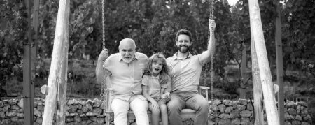 Men family weekend. Male generation family together with three different generations ages grandfather father and son having fun on a swing together in summer garden outdoors. Active family leisure
