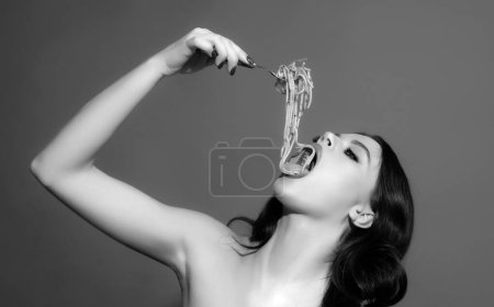 Téléchargez les photos : Cuisine italienne. Une fille qui mange des pâtes spaghetti. Manger des spaghettis à la fourchette. Aliments d'Italie - en image libre de droit