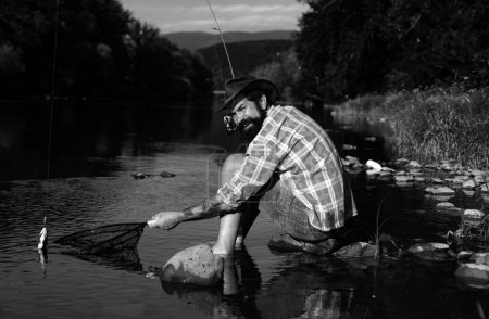Téléchargez les photos : Pêcheur pêchant sur un rever. Pêcheur détendu homme avec une canne à pêche un jour d'été. Pêcher la truite - en image libre de droit