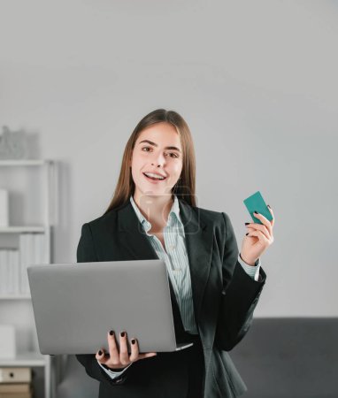 Financial services, credit card banking concept. Manager holding laptop computer and credit card indoors in office. Young business woman financial planning