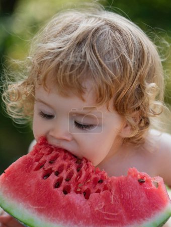 Photo for Happy child eating watermelon. Child baby eating watermelon in the garden, closeup face. Kid eat fruit outdoors. Kid baby playing in the garden biting a slice of watermelon - Royalty Free Image