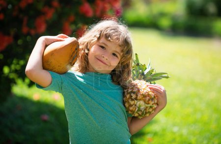 Téléchargez les photos : Joli gosse avec ananas et noix de coco au jardin tropical. Fruits tropicaux frais pour les enfants. Mode de vie sain avec des fruits tropicaux biologiques frais - en image libre de droit