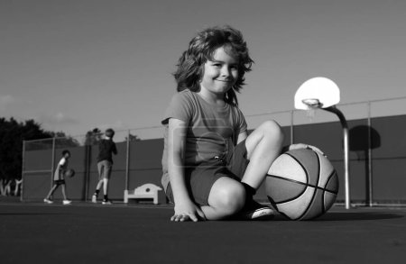 Téléchargez les photos : Joyeux petit garçon jouant au basket sur une aire de jeux - en image libre de droit
