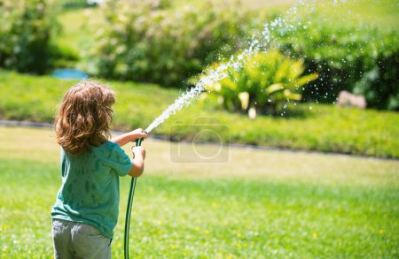 Téléchargez les photos : Les enfants jouent avec le tuyau d'arrosage dans la cour. Plein air enfants plaisir d'été. Petit garçon jouant avec un tuyau d'eau dans la cour. Jeu de fête pour les enfants. Activité saine pour une journée chaude et ensoleillée - en image libre de droit