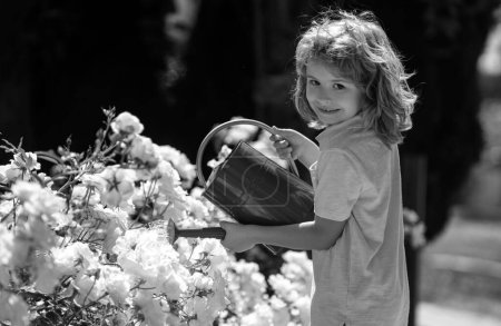 Foto de Lindo niño pequeño riego plantas con regadera en el jardín. Niño ayudando a los padres a cultivar flores en el patio. Actividades con niños al aire libre - Imagen libre de derechos