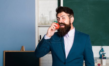 Téléchargez les photos : Le prof mange des pommes. Professeur souriant au tableau noir de la classe - en image libre de droit