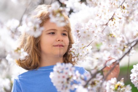 Photo for Kids face with flower on the Spring. Child in blooming cherry garden on beautiful spring day. Happy child during spring blossom. Kid in flowered garden. Outdoor Portrait of child near blossoming tree - Royalty Free Image