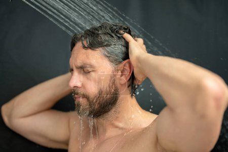 Foto de Hombre lavando el pelo en el baño. Cabezal de ducha en la bañera. Cara en espuma en la ducha. Bañista duchándose. Un tipo cercano duchándose. Concepto ducha. El hombre está bajo las gotas de agua en las duchas - Imagen libre de derechos