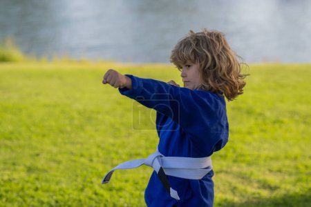 Photo for Kid boy in kimono practicing judo, taekwondo, jujitsu, kung-fu, jiu-jitsu, aikido outdoor. Sport karate kids. Little boy wearing kimono doing karate in park. Martial arts for kids - Royalty Free Image
