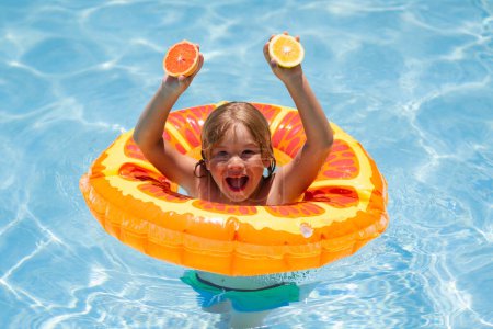 Téléchargez les photos : Enfant nageant dans la piscine. Vacances d'été. Enfant heureux jouant avec anneau de natation coloré dans la piscine le jour de l'été. Enfant avec orange dans la piscine. Fruits d'été - en image libre de droit