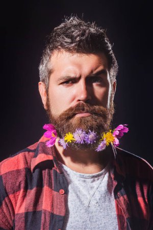 Foto de Un hombre barbudo con barba decorada para las vacaciones de primavera. Flor en la barba. Tendencias Faciales de Primavera. Productos de cuidado de belleza barba. Cosméticos para hombre barbudo con bigote - Imagen libre de derechos