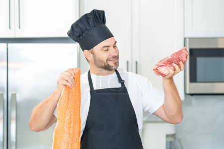 Téléchargez les photos : Homme d'âge moyen cuisiner du poisson et de la viande, du saumon et du bœuf dans la cuisine. Homme de cuisine avec poisson et viande, saumon et boeuf - en image libre de droit