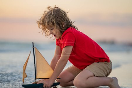 Téléchargez les photos : Enfant voyageant en mer. Enfant profitant de vacances d'été en bord de mer. Un petit garçon mignon jouant avec un bateau jouet sur la plage par une chaude journée ensoleillée d'été. Vacances en mer. Journée des enfants - en image libre de droit
